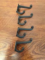 Five black cast iron hooks laid out on wood surface, front view