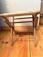 Stool folded partway showing wood frame and canvas seat