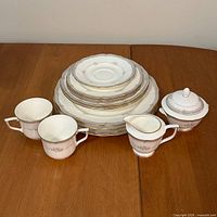 Stacked plates, bowls, two cups, creamer and lidded sugar bowl displayed on table