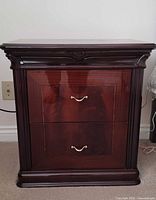 Front view of one night table showing two drawers, brass-tone handles and cherry wood finish