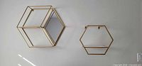 Two gold metal hexagon wall shelves, one mirrored cube style, one open frame