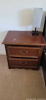 Front view of wood night table showing two drawers and lamp for scale