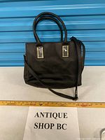 Front view of black satchel with strap and ruler for scale