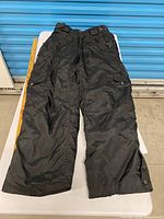 Full view of black insulated snow pants laid flat, showing front, pockets, leg openings