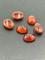 Six oval red garnet cabochons on dark background