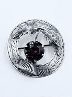 Front view of sterling silver thistle brooch with purple faceted glass stone