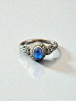 Front view showing blue oval stone, bezel, and filigree shoulders