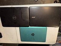 Three closed laptops showing lids with Dell, Acer, HP logos