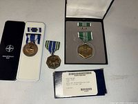 Four medals displayed: NATO ISAF medal in case, loose NATO Afghanistan medal, Army Achievement Medal set in case, sealed Afghanistan Campaign Medal package