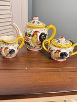 Front view of teapot, sugar bowl and creamer showing rooster motif and overall form