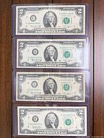 Four $2 bills in plastic sleeves displayed vertically