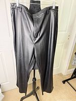 Full front view of black faux leather pants on hanger showing overall style and length