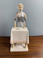 Full view of figurine showing woman, table, candles, and tablecloth