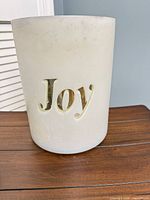 Full view of cylindrical frosted glass candle holder showing "Joy" cutout