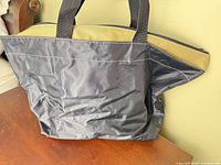 Front view of black nylon tote with beige band and straps visible