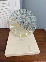 Front view of round glass plate on stand atop branded box