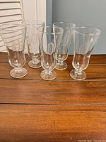 All five clear footed pilsner glasses displayed upright on wood surface