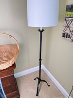 Full view of black metal floor lamp with white drum shade