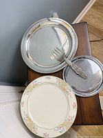 Group showing porcelain plate, large silver platter, small silver tray, serving fork