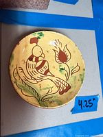 Full view of yellow redware plate with bird and tulip decoration, tape showing 4.25 in