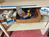Shelving with cardboard box of wire nuts, fittings, pliers, blue electrical box, plus boxed Lutron receptacles