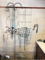 Overall lot hanging on wall: tall trellis, shepherd’s hooks, cages, stakes