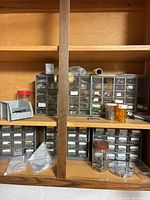 Wide view of shelf with multiple plastic drawer organizers, jars and hardware