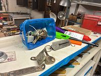 Blue bin containing padlocks with keys, multicolour butane lighters, background metal box