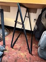 Full view of one black folding metal table support under tabletop