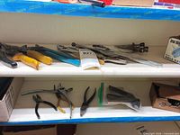 Shelf with multiple pliers and snips on upper shelf; additional pliers, bagged parts and boxes on lower shelf