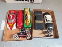 All six items arranged in two trays: red #94 stock car, red streamlined car, Texaco bus bank, Model T style Texaco car, black sedan, black/white police car