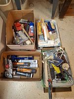 Four boxes containing paint brushes, stir sticks, roller frames, trays, caulking tubes, scrapers