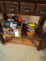 Spray paint cans in cardboard box next to gallon polyurethane can