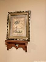 Wood wall shelf mounted under large framed palm print