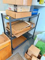 Front view of black metal shelf with two shelves, cardboard boxes on and around it (contents not included)