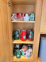 Cabinet view showing three shelves of assorted Starbucks mugs, various colors and heights