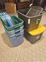 Stack of three blue-green totes with four lids beside two nested black totes, one with yellow lid