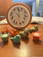 Front view of wall clock, four ceramic bird figurines, three flower-shaped votive holders with candles