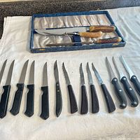 Boxed carving knife and fork with antler handles plus array of 13 steak knives on cloth