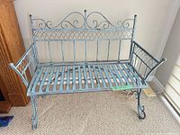 Front view of turquoise cast iron bench showing ornate back, slatted seat, scroll arms, and dimensions tag