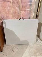 Table folded and standing upright showing overall appearance and carry handle