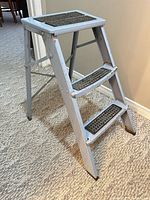 Side view of light blue metal three-step folding stool ladder on carpet