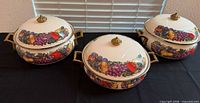 Three covered enamel serving pieces with fruit motif displayed with lids on