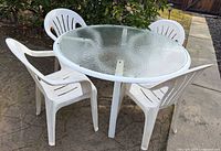 Full view of round glass-top table with four white plastic patio chairs