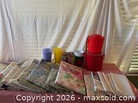 Folded tablecloths, two red ice buckets, assorted plastic cups