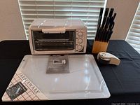Overall view of toaster oven, sealed cutting board, knife block with knives, measuring spoons