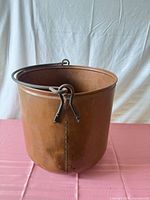 Front view of copper bucket showing patina and iron handle brackets