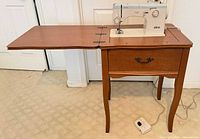 Elna machine mounted in cabinet with leaf extended, foot pedal visible