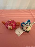 Two miniature ceramic teapots, pink floral and white with cat design