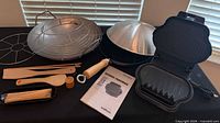 Group shot showing wok with rack and lid, George Foreman grill, bamboo utensils, skewers and manual
